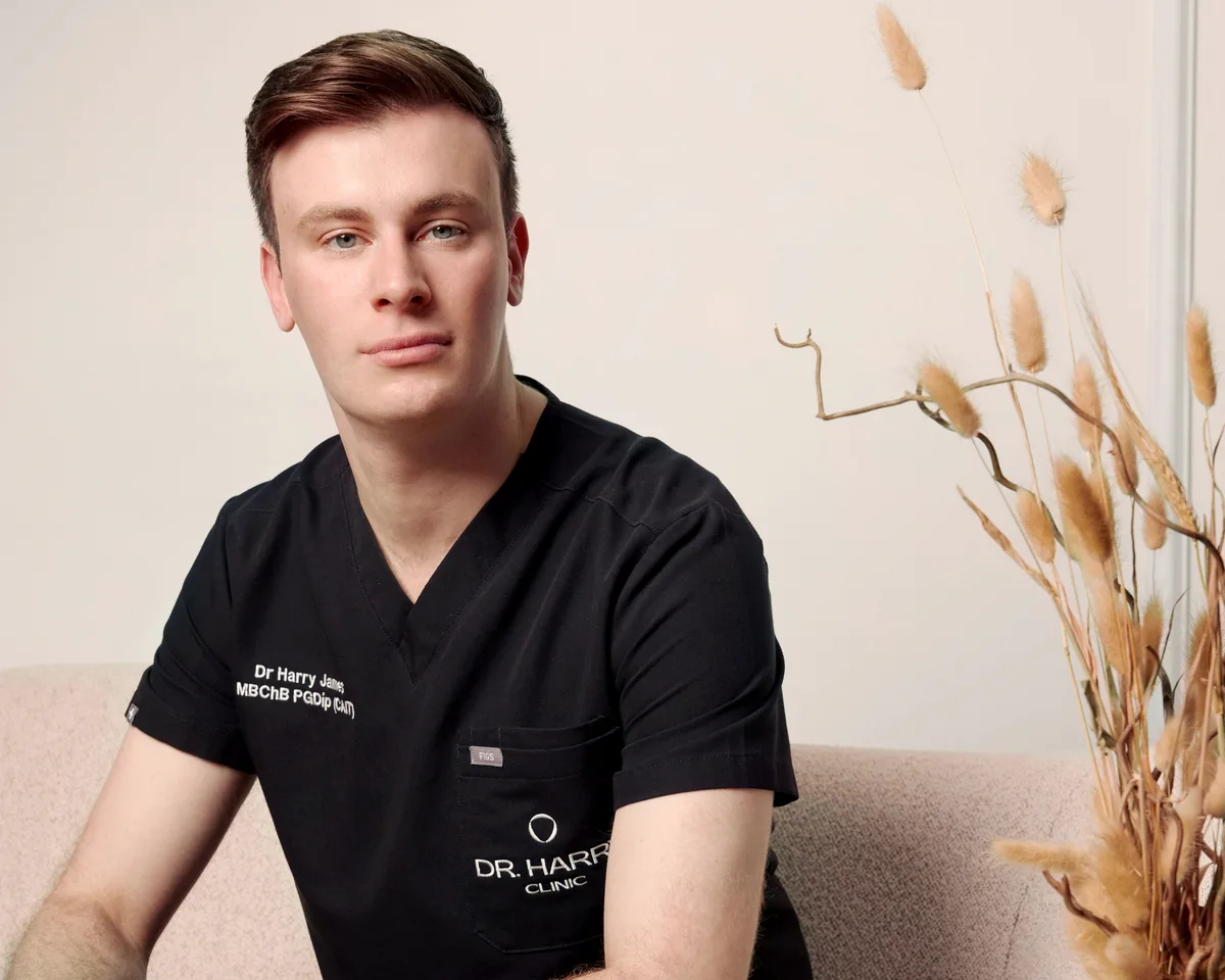 Close portrait of Dr Harry James on the clinic sofa, clinic scrubs embroidered with his name and qualifications.