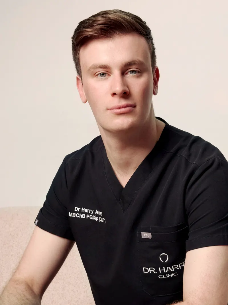 Close portrait of Dr Harry James on the clinic sofa, clinic scrubs embroidered with his name and qualifications.